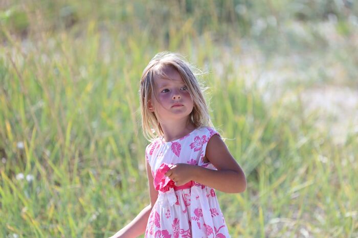 Young girl in a floral dress stands outdoors, looking curious.