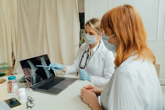 Doctor in mask explaining X-ray results to patient, representing unexplainable pain people endure in a clinical setting