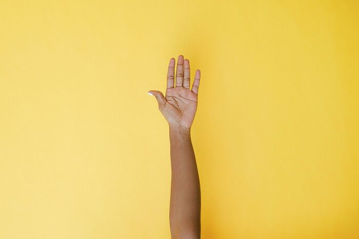 Raised hand against a yellow background, symbolizing sharing intrusive thoughts.