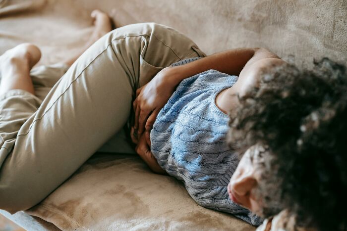 Person lying curled up on a couch holding their abdomen, showing unexplainable pain.