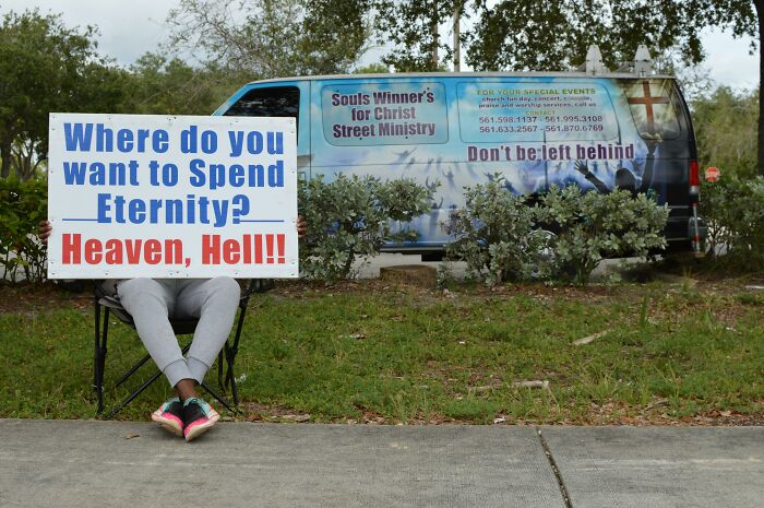 Person holding a sign about eternity and hell outside a church van with messages that caused people to quit going.