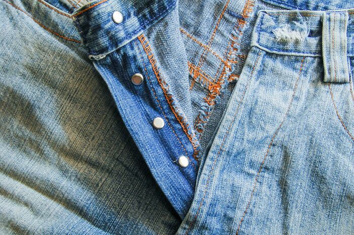 Close-up of distressed denim jeans with button detail and frayed edges, illustrating casual fashion.