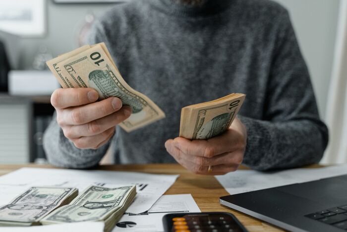 Person counting U.S. dollars at a desk with papers, reflecting an interesting American habit.
