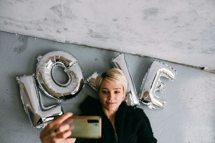 Person taking a selfie with silver "LOVE" balloons, sharing thoughts in a casual setting.