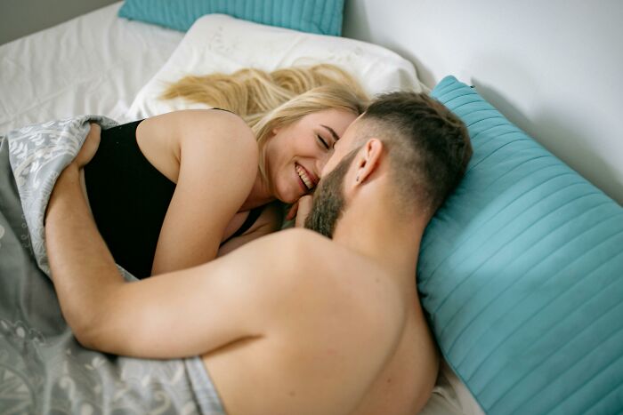 A couple in bed smiling and embracing, reflecting relationship insights guys discover after getting a girlfriend.