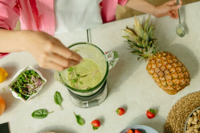 Person prepares a green smoothie with pineapple and strawberries, an example of people sharing unique recipe thoughts.