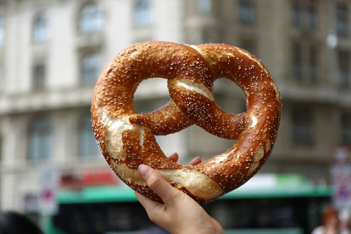 Hand holding a large pretzel against an urban backdrop, symbolizing the art of skillful insults.