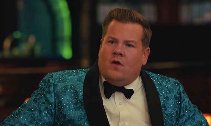 Man in a sparkling blue suit and bow tie in a dimly lit room, involved in a conversation. Hollywood casting regrets.