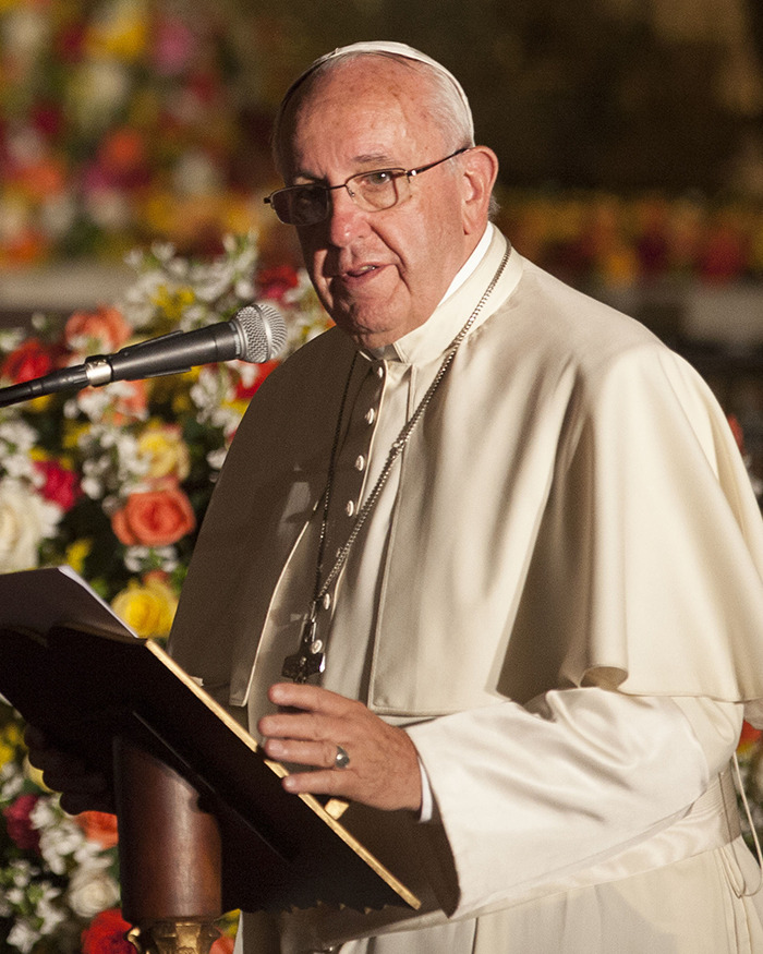 Pope Francis speaking at an event, wearing traditional papal attire, with floral decor in the background. Pope Francis speaking at an event, wearing traditional papal attire, with floral decor in the background.