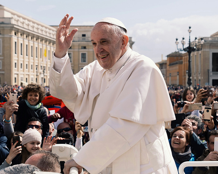 Man in white robe greeting crowd in outdoor setting, surrounded by smiling people and cameras. Man in white robe greeting crowd in outdoor setting, surrounded by smiling people and cameras.