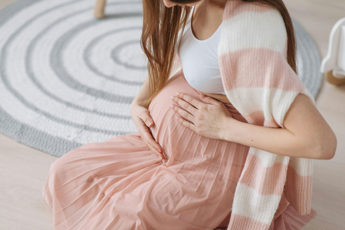 Pregnant woman in a pink skirt sitting on the floor, gently touching her belly. Pregnant woman in a pink skirt sitting on the floor, gently touching her belly.