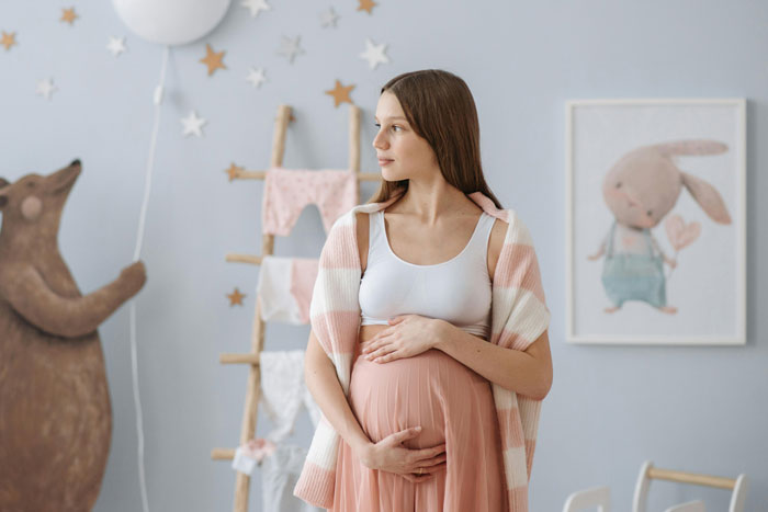Pregnant woman in a pastel-themed nursery, gently holding her belly, surrounded by whimsical decor. Pregnant woman in a pastel-themed nursery, gently holding her belly, surrounded by whimsical decor.
