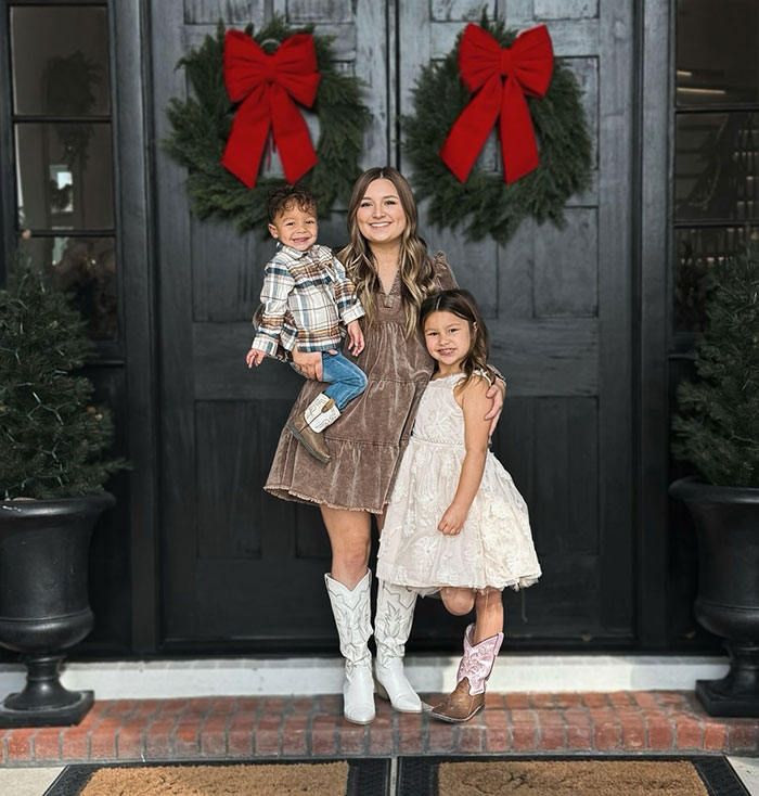 Woman with two children, holiday wreaths on door, memorializing TikTok star 'Okay Baby' in heartfelt setting. Woman with two children, holiday wreaths on door, memorializing TikTok star 'Okay Baby' in heartfelt setting.