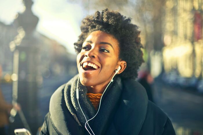 A woman smiling outdoors, wearing earphones, enjoying her day.