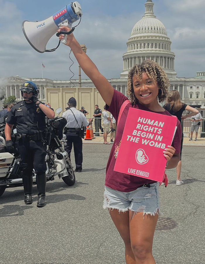 Pro-life activist holds megaphone and sign reading "Human Rights Begin in the Womb" near the Capitol building. Pro-life activist holds megaphone and sign reading "Human Rights Begin in the Womb" near the Capitol building.