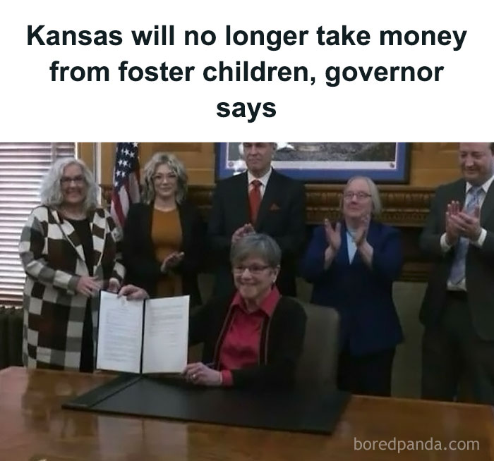 Governor signing document surrounded by applauding officials, addressing foster children funding policy.