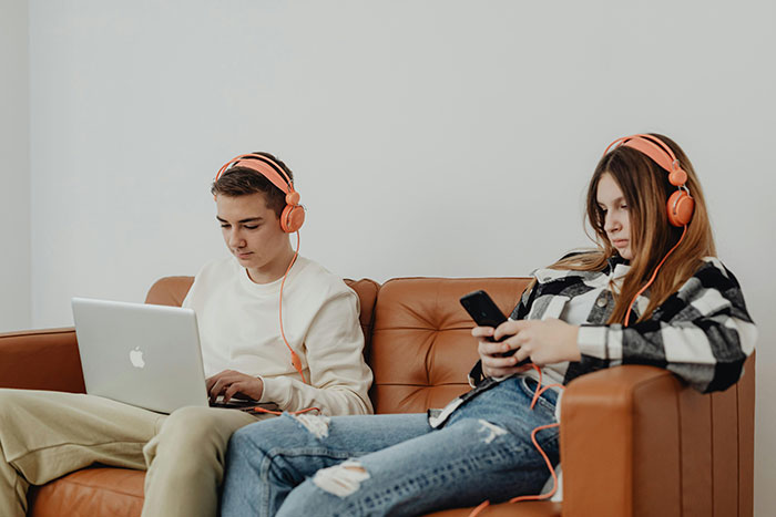 Two teens with headphones, one using a laptop and the other a phone, embodying entitled attitude and parental challenges. Two teens with headphones, one using a laptop and the other a phone, embodying entitled attitude and parental challenges.