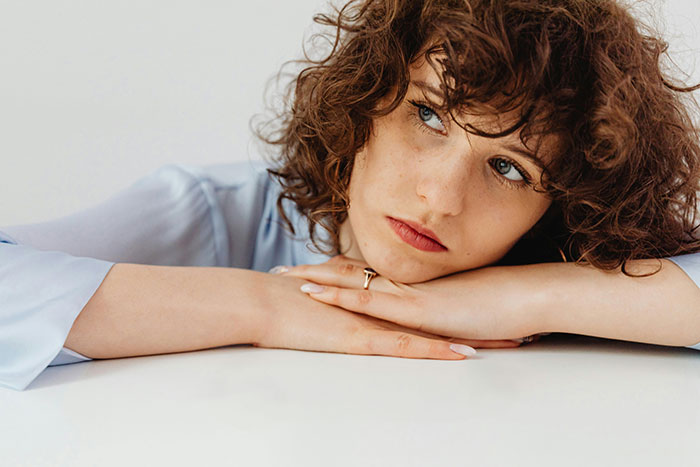 Curly-haired teen looking pensive, head resting on arms on a table. Curly-haired teen looking pensive, head resting on arms on a table.