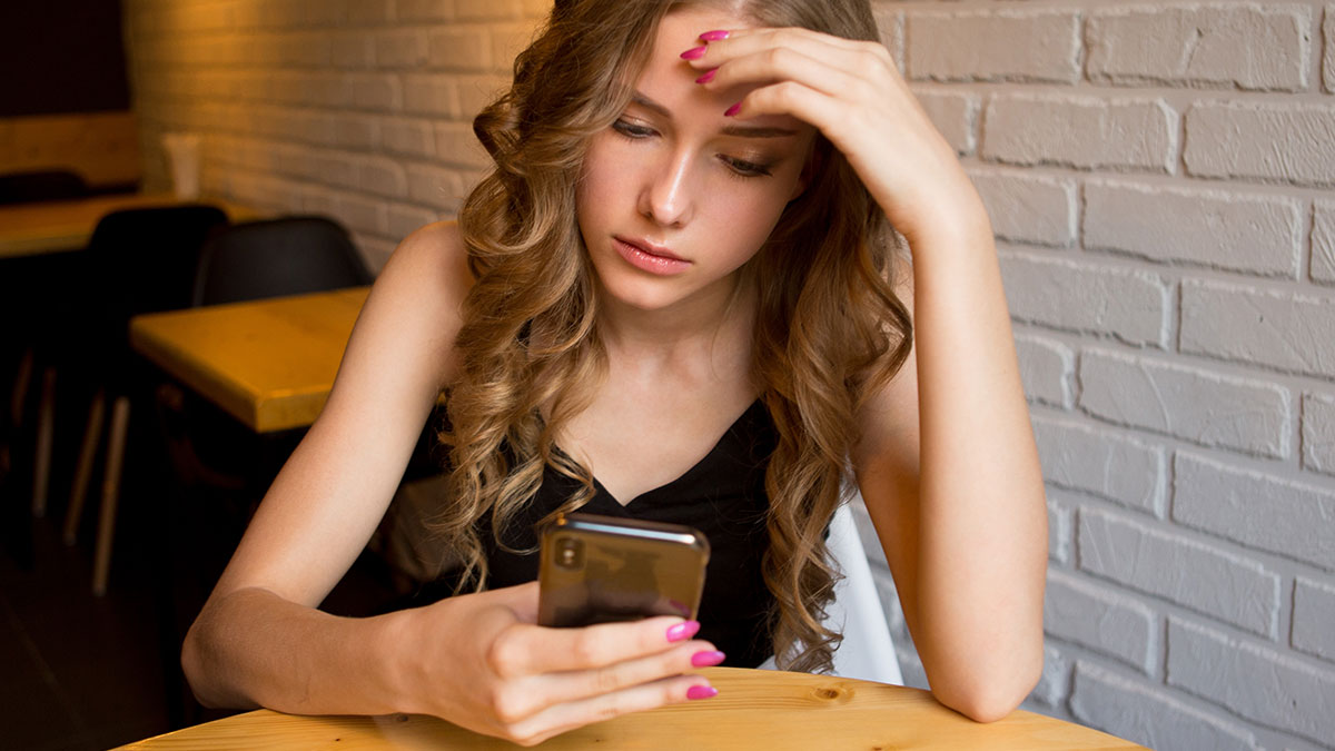 Young woman looking concerned at her smartphone, reflecting friendship in shambles after hygiene accusations.