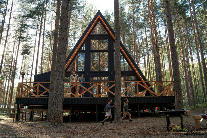 Girl with leukemia watching for bears outside cabin in forest at dusk while her father looks on and children run nearby.