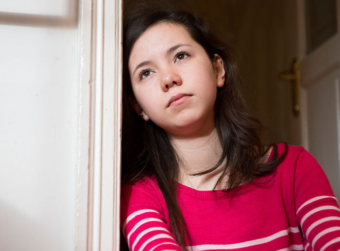 Young girl in a pink sweater appears contemplative, her eating disorder is discussed online by parents; leaning against a door. Young girl in a pink sweater appears contemplative, her eating disorder is discussed online by parents; leaning against a door.