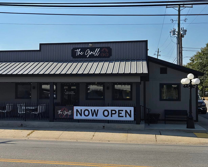 Front view of The Grill restaurant with a "Now Open" sign on the facade. Front view of The Grill restaurant with a "Now Open" sign on the facade.