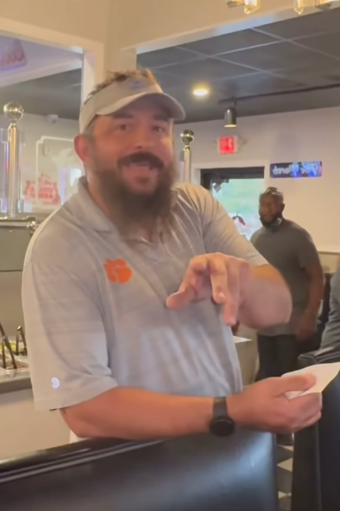 Restaurant owner in a grey polo, pointing and holding paper, in a casual dining setting. Restaurant owner in a grey polo, pointing and holding paper, in a casual dining setting.