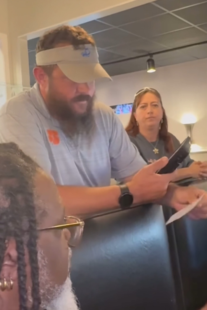 Restaurant owner reading a note, holds a phone; staff looks on, highlighting unprofessional customer-shaming incident. Restaurant owner reading a note, holds a phone; staff looks on, highlighting unprofessional customer-shaming incident.