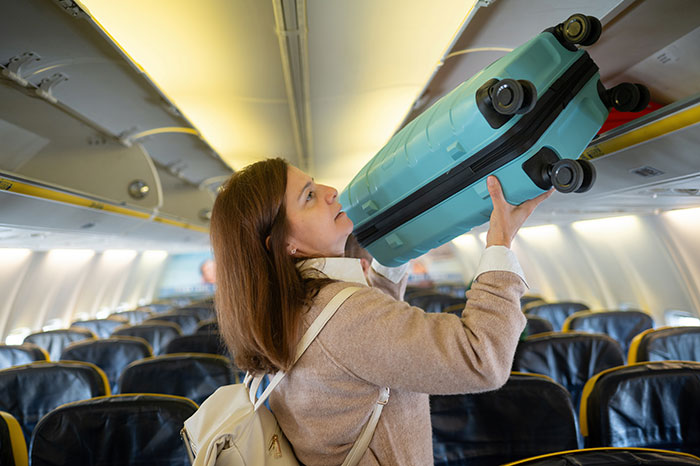 Woman placing luggage in overhead compartment on a plane, illustrating perfect revenge travel scenario. Woman placing luggage in overhead compartment on a plane, illustrating perfect revenge travel scenario.