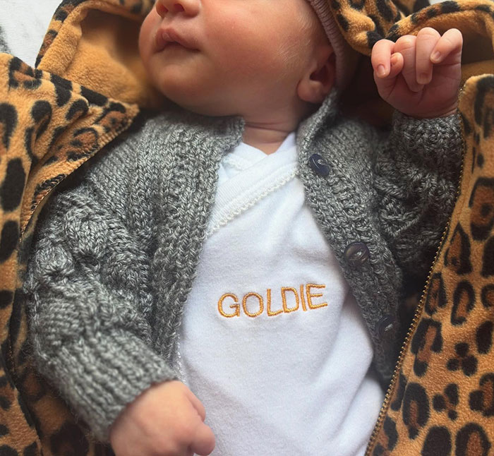 Rupert Grint's baby daughter Goldie in a grey sweater and personalized onesie, nestled in a leopard print blanket. Rupert Grint's baby daughter Goldie in a grey sweater and personalized onesie, nestled in a leopard print blanket.