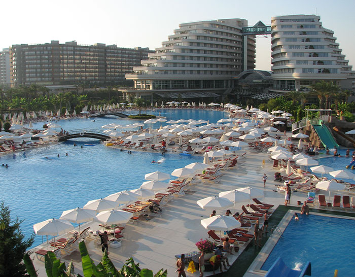 5-star resort in Turkey with a large pool, sunbathing chairs, and umbrellas crowded with guests enjoying the amenities. 5-star resort in Turkey with a large pool, sunbathing chairs, and umbrellas crowded with guests enjoying the amenities.