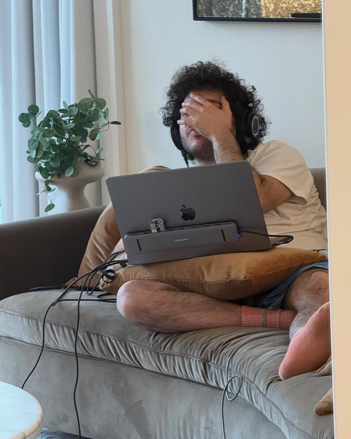 Person sitting on a couch with headphones, laptop on the lap. Surrounded by household items, creating an intimate setting. Person sitting on a couch with headphones, laptop on the lap. Surrounded by household items, creating an intimate setting.