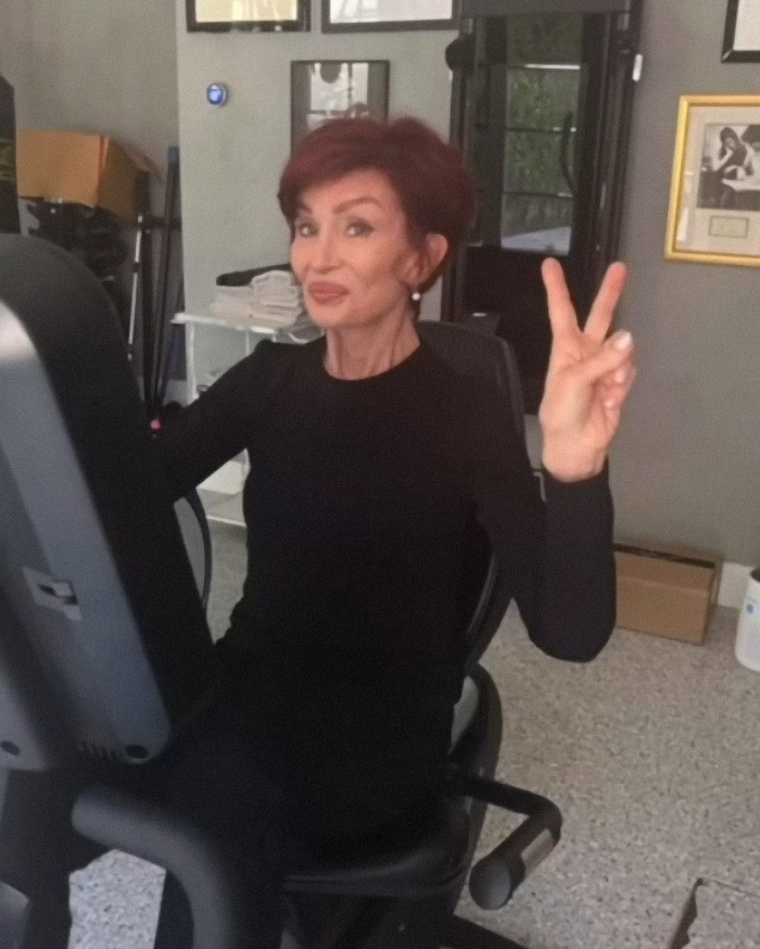 Woman on exercise bike, smiling and gesturing peace sign, amidst filter controversy in family photo. Woman on exercise bike, smiling and gesturing peace sign, amidst filter controversy in family photo.