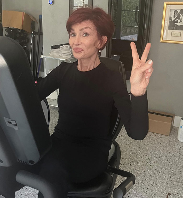Woman on exercise bike in black outfit, making peace sign, related to discussion on "Ozempic Feet" side effect. Woman on exercise bike in black outfit, making peace sign, related to discussion on "Ozempic Feet" side effect.