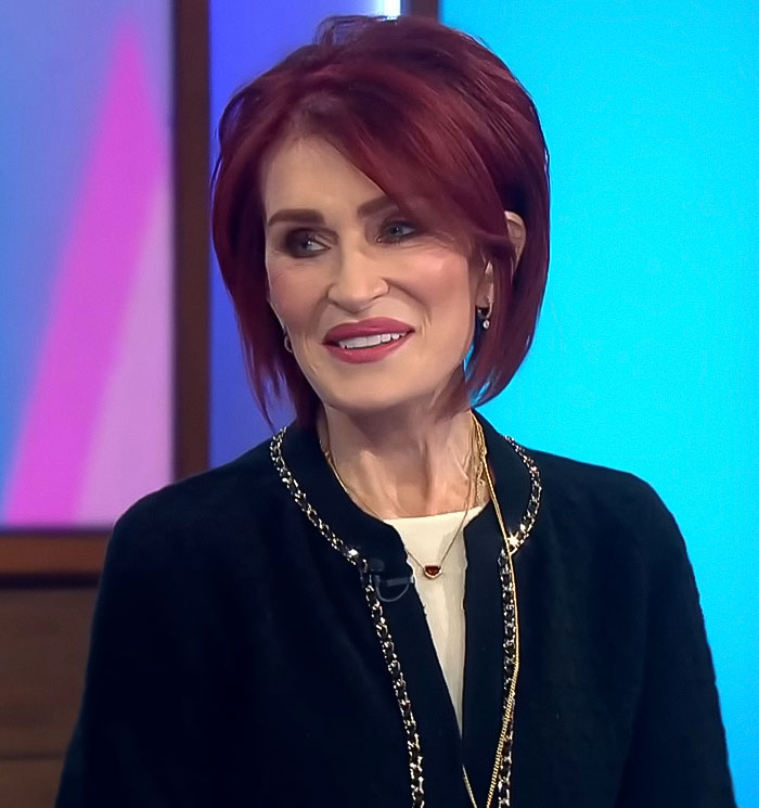 A woman with red hair in a black jacket speaks on a blue background, related to Ozempic feet side effect. A woman with red hair in a black jacket speaks on a blue background, related to Ozempic feet side effect.