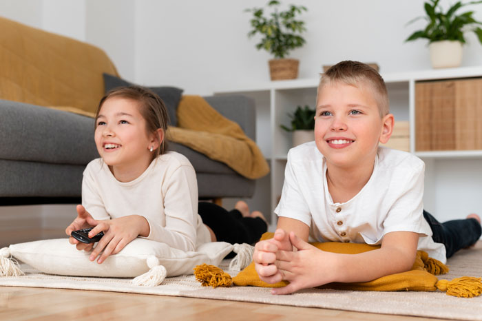 Children relaxing on cushions, watching TV together in a cozy living room setting. Children relaxing on cushions, watching TV together in a cozy living room setting.