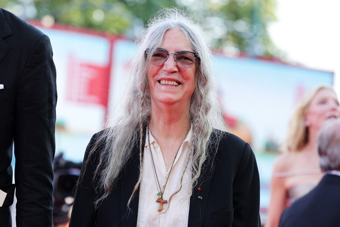 Punk rock legend smiling outdoors, wearing glasses and a black jacket. Punk rock legend smiling outdoors, wearing glasses and a black jacket.