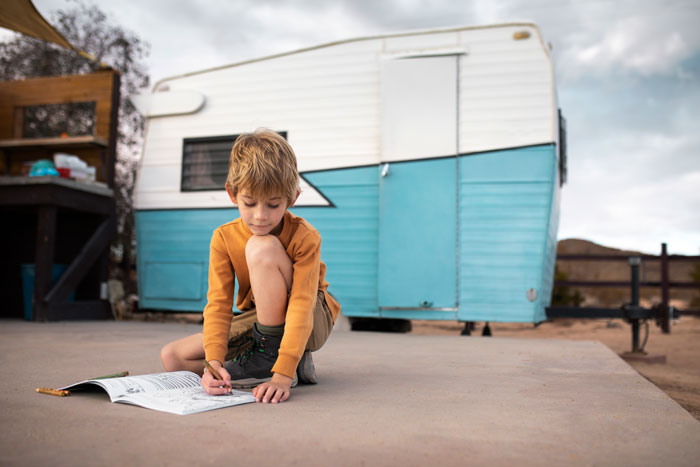 Child drawing outdoors near a blue and white trailer, focusing intently. Child drawing outdoors near a blue and white trailer, focusing intently.