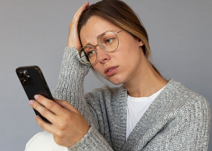 A worried woman with glasses looking at her phone, regretting family drama and $2,000 damages. A worried woman with glasses looking at her phone, regretting family drama and $2,000 damages.