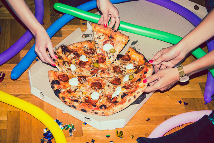 Hands reaching for pizza at a sleepover with colorful balloons scattered on the floor. Hands reaching for pizza at a sleepover with colorful balloons scattered on the floor.