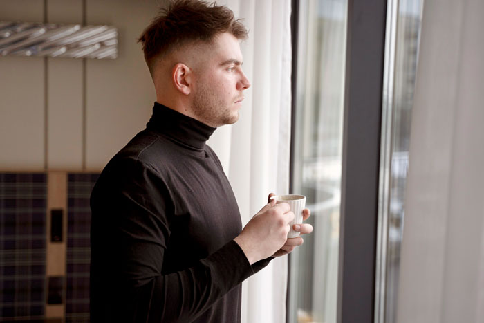 Teen boy in black turtleneck holding cup, looking out window thoughtfully, capturing moment related to dad catching son creeping. Teen boy in black turtleneck holding cup, looking out window thoughtfully, capturing moment related to dad catching son creeping.