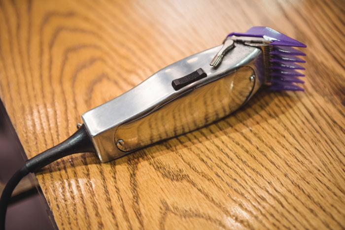 Electric hair clipper with purple attachment resting on a wooden surface, related to son father grooming drama. Electric hair clipper with purple attachment resting on a wooden surface, related to son father grooming drama.