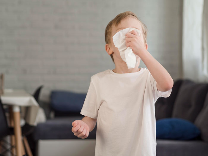 Young boy with allergies wipes face with tissue in living room. Young boy with allergies wipes face with tissue in living room.