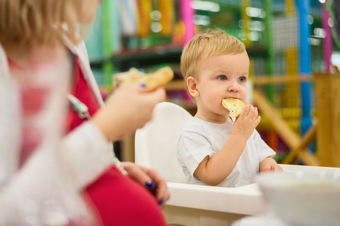 Toddler in a high chair eating bread, potential allergy concerns highlighted by father's question. Toddler in a high chair eating bread, potential allergy concerns highlighted by father's question.