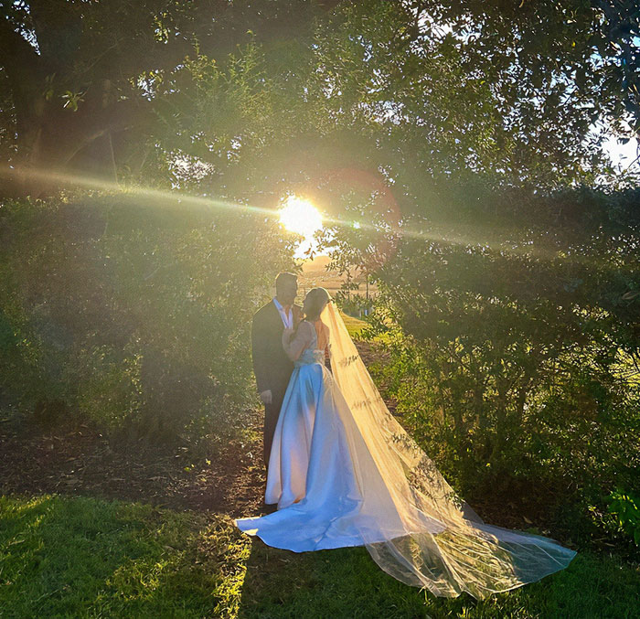 Burns survivor at wedding with partner, sunlight streaming through trees, creating a magical backdrop. Burns survivor at wedding with partner, sunlight streaming through trees, creating a magical backdrop.