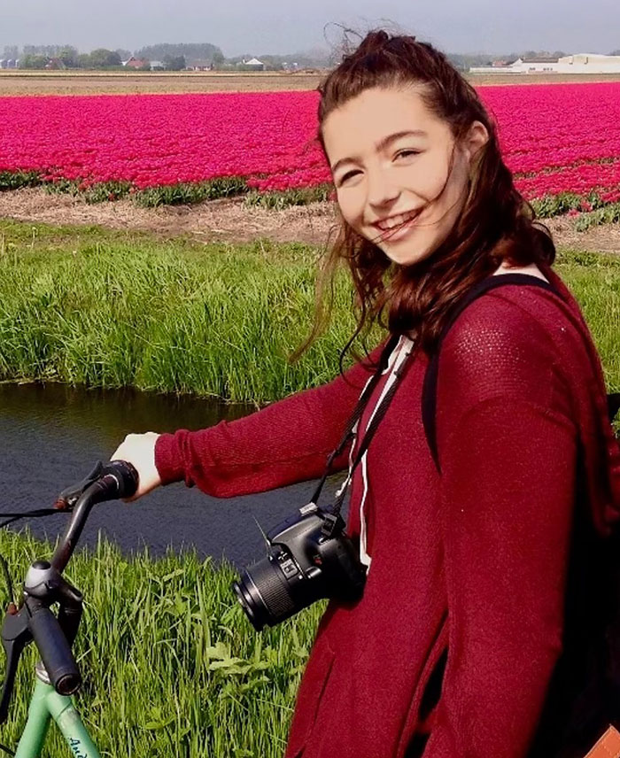 Former child star smiling on a bicycle, wearing a red sweater, with a camera around her neck in a flower field. Former child star smiling on a bicycle, wearing a red sweater, with a camera around her neck in a flower field.