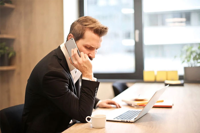 Businessman on a phone call at his desk, appearing focused on resolving spam caller issue. Businessman on a phone call at his desk, appearing focused on resolving spam caller issue.
