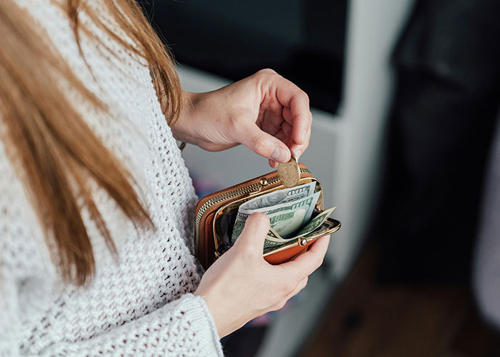 Woman in a knitted sweater handling cash and coins from a wallet, symbolizing overcharged rent. Woman in a knitted sweater handling cash and coins from a wallet, symbolizing overcharged rent.