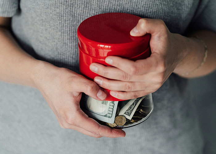 Person holding a jar with cash and coins, symbolizing overcharged rent for chores. Person holding a jar with cash and coins, symbolizing overcharged rent for chores.