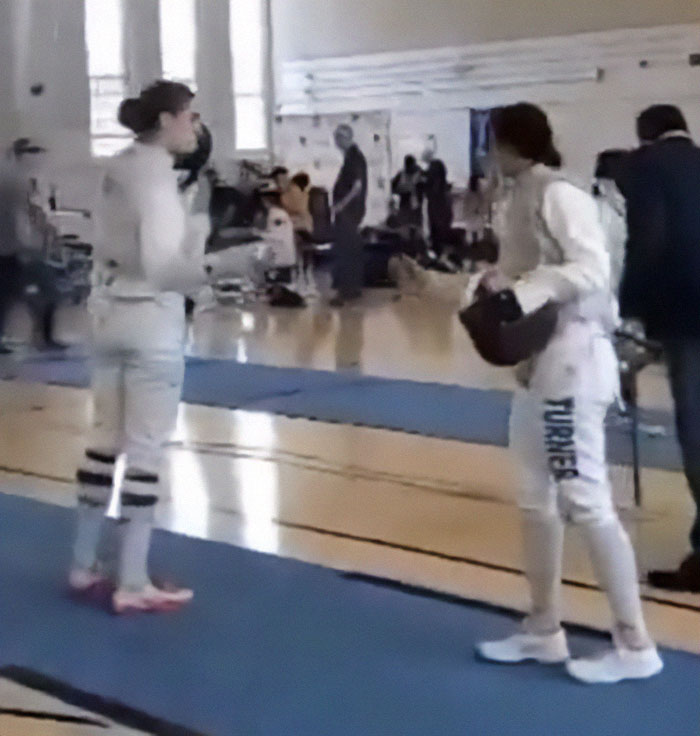 Two fencers in a gym engaged in conversation during a college fencing event. Two fencers in a gym engaged in conversation during a college fencing event.